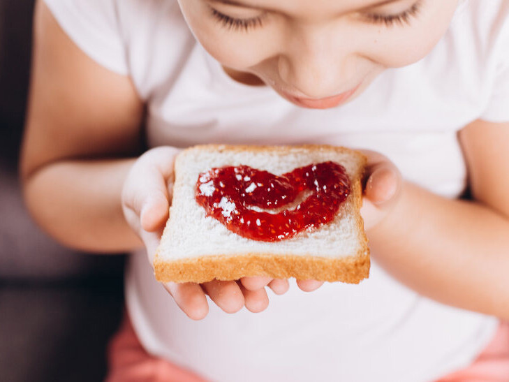 A child is holding a slice of bread with jelly spread in the shape of a heart.