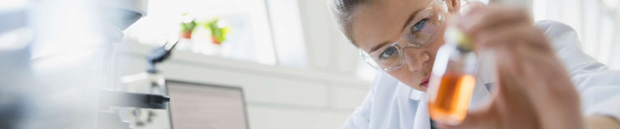 Woman in a lab holding a little bottle with orange fluid